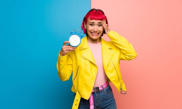 Mujer joven con chaqueta amarilla inquieta porque se ha hecho tarde y la celebración de reloj despertador vintage
 - Foto, Imagen