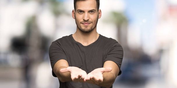Man met zwart shirt Holding copyspace denkbeeldige op de Palm om een advertentie invoegen in openlucht - Foto, afbeelding