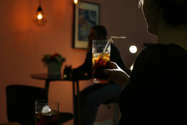 Woman with glass of cold cola in dark cafe, closeup. Space for text - Fotoğraf, Görsel