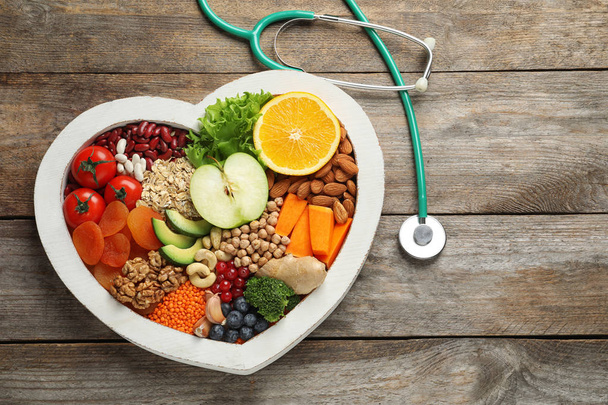 Heart shaped tray with healthy products and stethoscope on wooden background, top view. Space for text - Φωτογραφία, εικόνα