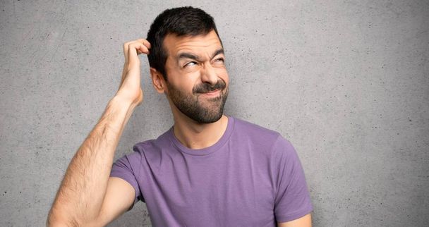 Handsome man having doubts while scratching head over textured wall - Photo, Image