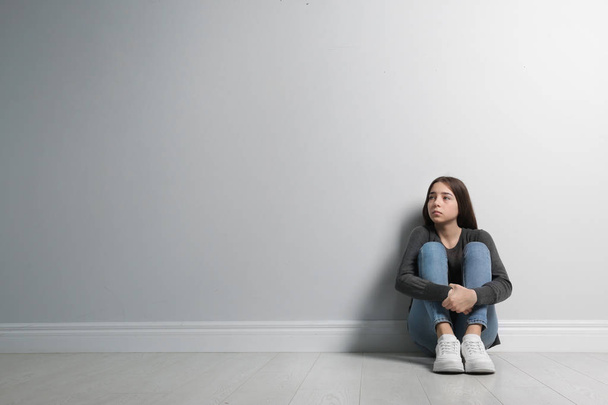 Upset teenage girl sitting on floor near wall. Space for text - Foto, Bild