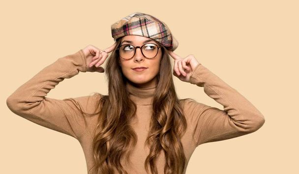 Young woman with beret having doubts and thinking over isolated yellow background - Photo, Image