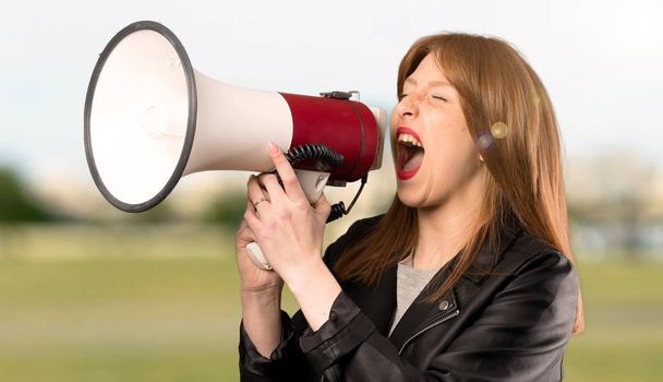 Young redhead woman shouting through a megaphone at outdoors - Photo, Image