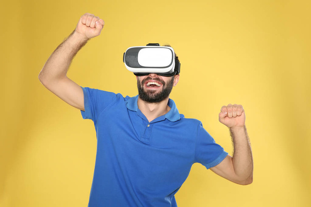 Emotional young man playing video games with virtual reality headset on color background - Foto, imagen