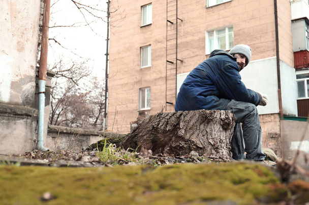 Poor homeless man sitting on stump outdoors - Fotó, kép