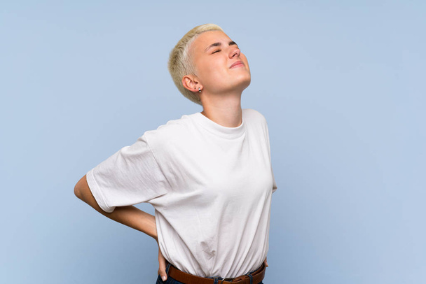 Adolescente aux cheveux courts blancs sur un mur bleu souffrant de maux de dos pour avoir fait un effort
 - Photo, image