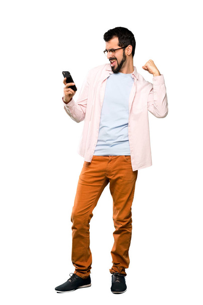 Full-length shot of Handsome man with beard with phone in victory position over isolated white background - Fotografie, Obrázek