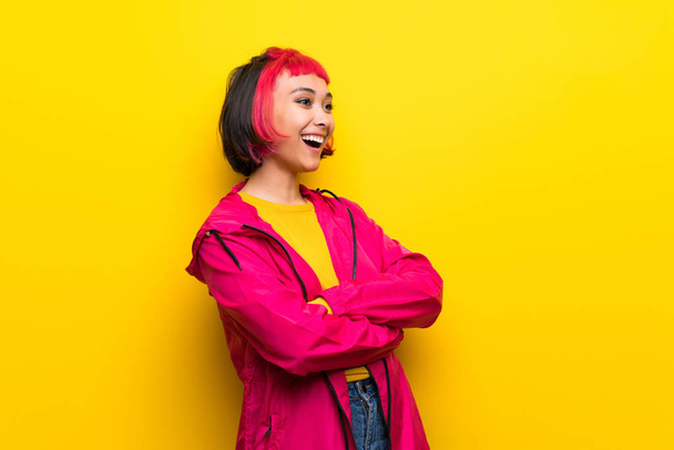 Jeune femme aux cheveux roses sur mur jaune heureux et souriant
 - Photo, image