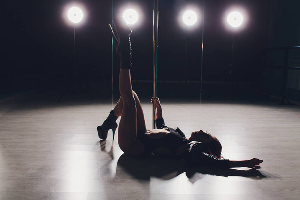 Red haired pole dance girl exercises and poses on the pylon in the smoke on the black background. - 写真・画像