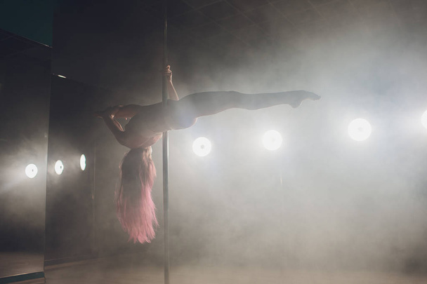 Young slim woman pole dancing in dark interior with lights and smoke. - Foto, imagen