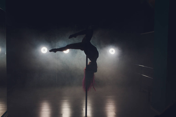 Young slim woman pole dancing in dark interior with lights and smoke. - Zdjęcie, obraz