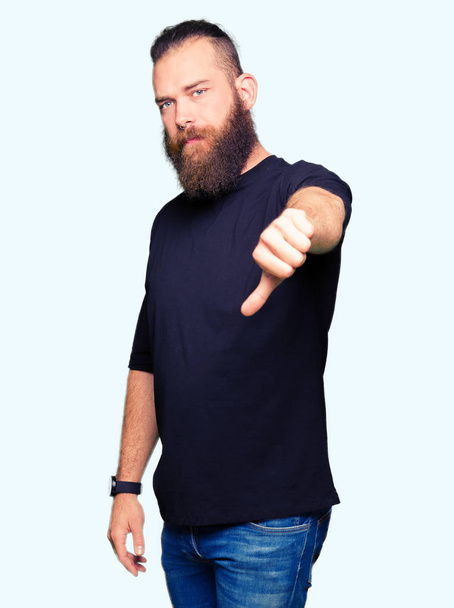 Young blond man wearing casual t-shirt looking unhappy and angry showing rejection and negative with thumbs down gesture. Bad expression. - Photo, image
