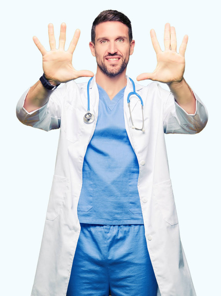Handsome doctor man wearing medical uniform over isolated background showing and pointing up with fingers number ten while smiling confident and happy. - Foto, imagen