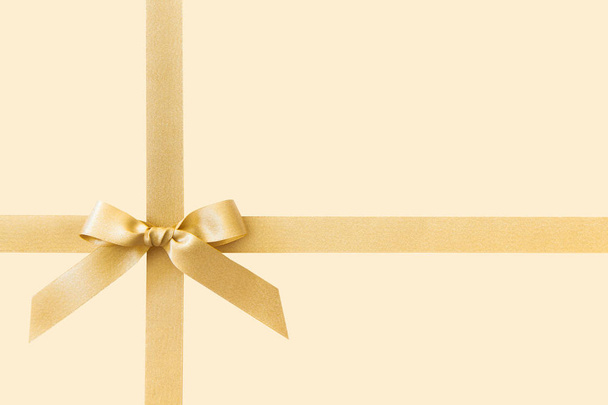 Gold ribbon with a bow as a gift on a beige background - Φωτογραφία, εικόνα