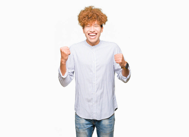 Young handsome business man with afro hair wearing elegant shirt very happy and excited doing winner gesture with arms raised, smiling and screaming for success. Celebration concept. - Fotografie, Obrázek
