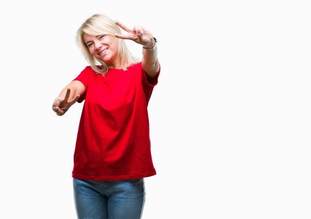 Νέοι όμορφη ξανθιά γυναίκα που φοράει κόκκινο t-shirt πέρα από το απομονωμένο υπόβαθρο χαμογελώντας ψάχνει στην κάμερα δείχνει τα δάχτυλα που κάνει το σήμα της νίκης. Αριθμός δύο. - Φωτογραφία, εικόνα