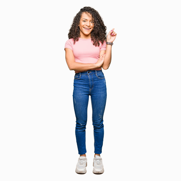Young beautiful woman with curly hair wearing pink t-shirt with a big smile on face, pointing with hand and finger to the side looking at the camera. - Foto, Imagem
