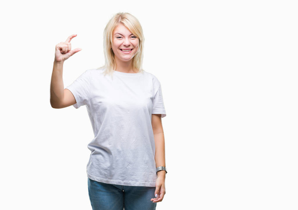 Giovane bella donna bionda indossa t-shirt bianca su sfondo isolato sorridente e fiducioso gesticolando con mano facendo segno dimensioni con le dita mentre si guarda e la fotocamera. Concetto di misura
. - Foto, immagini
