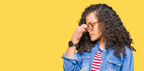 Young beautiful woman with curly hair wearing glasses tired rubbing nose and eyes feeling fatigue and headache. Stress and frustration concept. - Zdjęcie, obraz