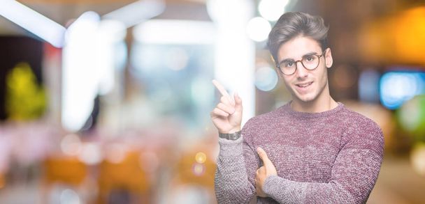 Young handsome man wearing glasses over isolated background with a big smile on face, pointing with hand and finger to the side looking at the camera. - Photo, image