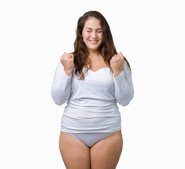 schöne plus size junge übergewichtige Frau in weißer Unterwäsche über isoliertem Hintergrund aufgeregt für den Erfolg mit erhobenen Armen feiern den Sieg lächelnd. Siegerkonzept. - Foto, Bild