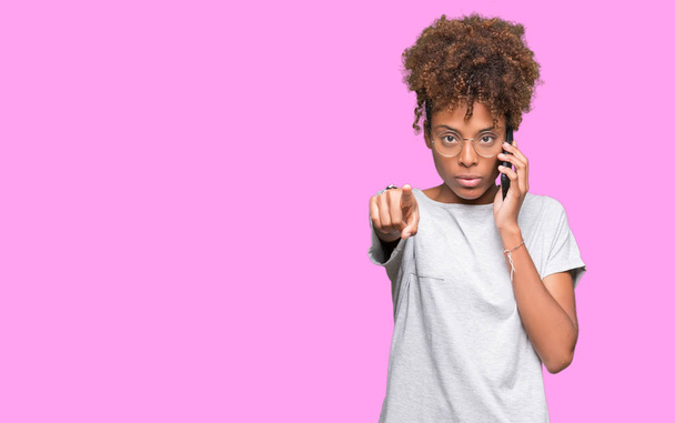 Νεαρός αφρικανική αμερικανική γυναίκα που μιλάνε στο smartphone απομονωμένοι φόντο δείχνοντας με το δάχτυλο στη φωτογραφική μηχανή και σε εσάς, το χέρι συνδεθείτε, θετική και σίγουρη κίνηση από το μέτωπο - Φωτογραφία, εικόνα