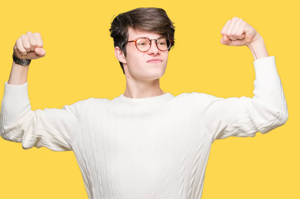 Joven hombre guapo con gafas sobre un fondo aislado que muestra los músculos de los brazos sonriendo orgulloso. Concepto Fitness
. - Foto, imagen