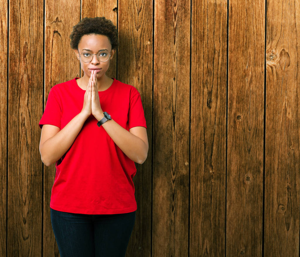 schöne junge afrikanisch-amerikanische Frau mit Brille über isoliertem Hintergrund betet mit den Händen zusammen und bittet um Vergebung lächelt zuversichtlich. - Foto, Bild