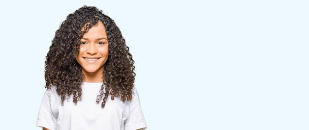 Young beautiful woman with curly hair wearing white t-shirt with a happy and cool smile on face. Lucky person. - Photo, Image