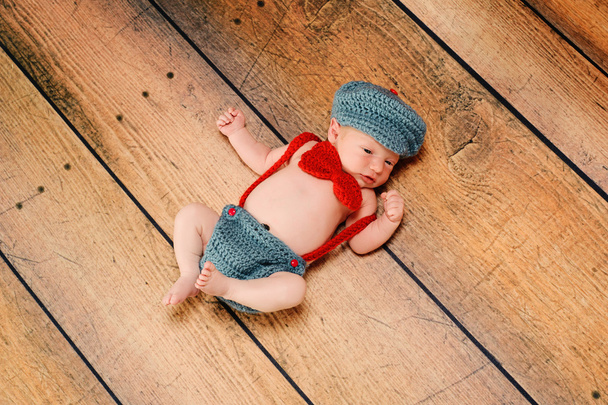 pasgeboren babyjongen dragen een vintage geïnspireerd grijze en rode kleine man pak bestaande uit bretels, vlinderdas en krantenverkoper hoed. - Foto, afbeelding