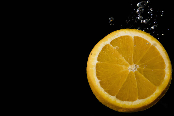 Zitronenscheibe in Wasser getaucht mit Blasen auf schwarzem Hintergrund - Foto, Bild