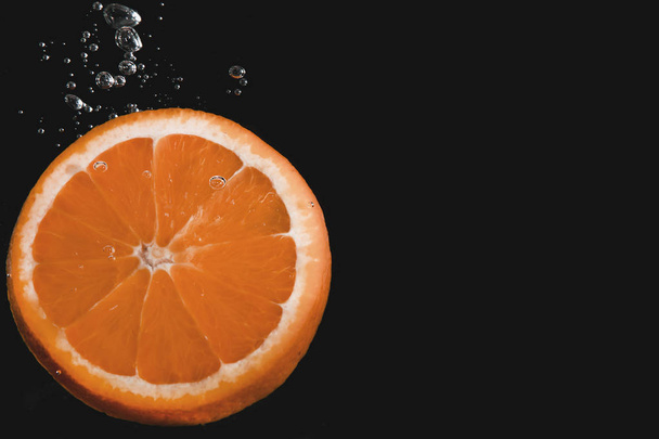 Tranche orange immergée dans l'eau avec des bulles sur fond noir
 - Photo, image