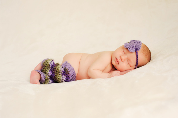Nouveau-né bébé fille portant violet et vert bonneterie jambières et bandeau et dormir sur une couverture de couleur crème
. - Photo, image