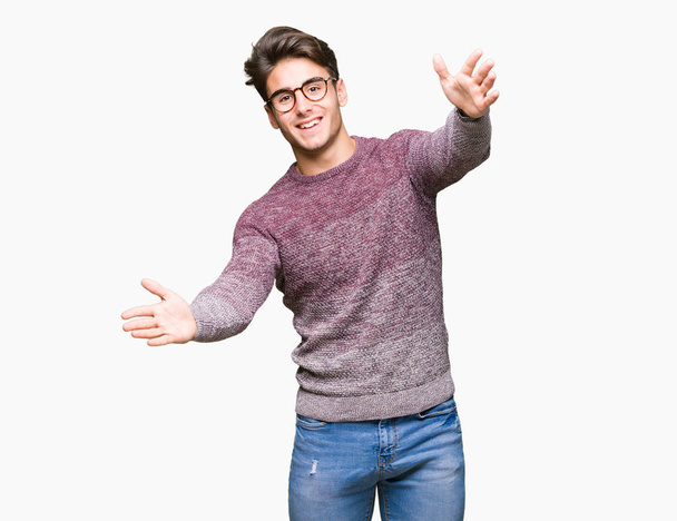 Young handsome man wearing glasses over isolated background looking at the camera smiling with open arms for hug. Cheerful expression embracing happiness. - Foto, imagen