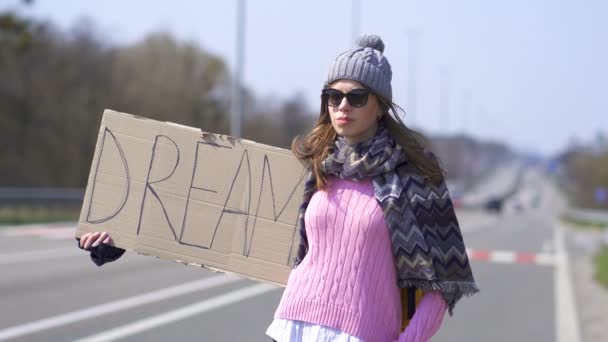 Młoda ładna kobieta autostopem zatrzymanie samochodu z marzeniem plakat.  - Materiał filmowy, wideo