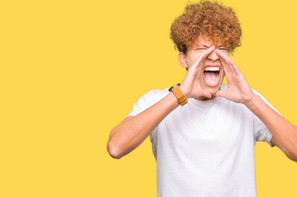 Young handsome man with afro hair wearing casual white t-shirt Shouting angry out loud with hands over mouth - Foto, imagen
