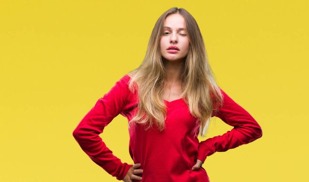 junge schöne blonde Frau trägt roten Pullover über isoliertem Hintergrund zwinkert in die Kamera mit sexy Ausdruck, fröhliches und glückliches Gesicht. - Foto, Bild