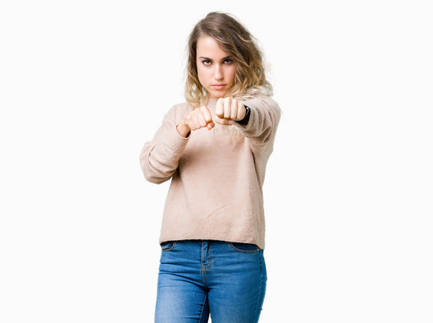 Beautiful young blonde woman wearing sweatershirt over isolated background Punching fist to fight, aggressive and angry attack, threat and violence - Foto, Bild