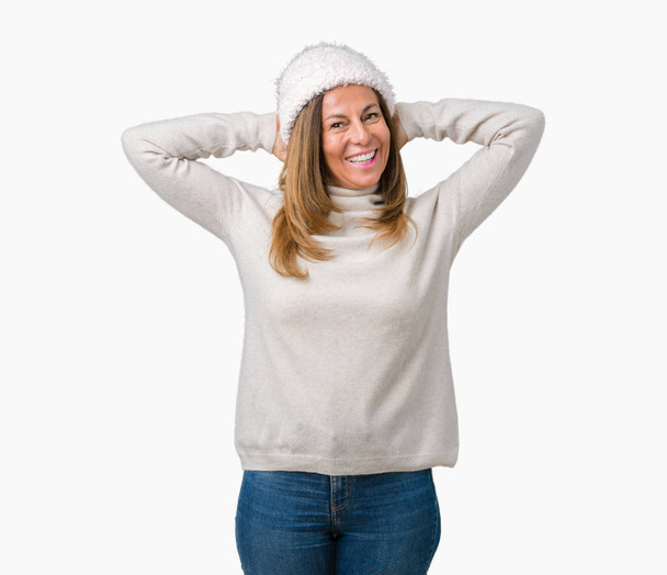 Beautiful middle age woman wearing winter sweater and hat over isolated background Relaxing and stretching with arms and hands behind head and neck, smiling happy - Фото, изображение