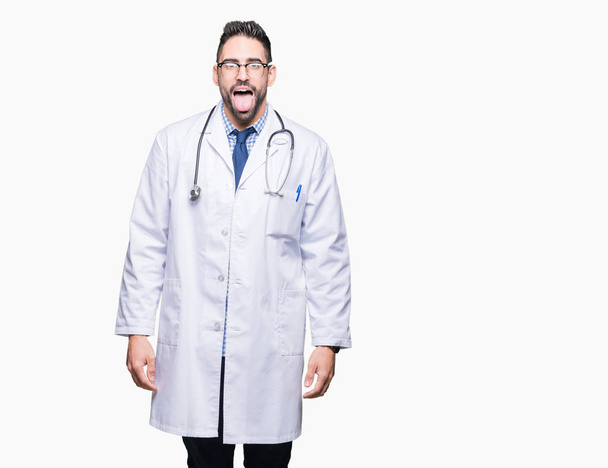 Handsome young doctor man over isolated background sticking tongue out happy with funny expression. Emotion concept. - Fotó, kép