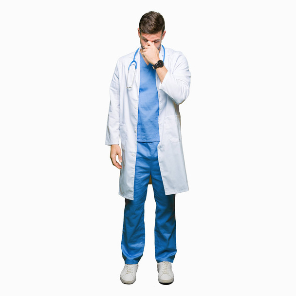 Hombre guapo doctor vistiendo uniforme médico sobre fondo aislado cansado frotando la nariz y los ojos sintiendo fatiga y dolor de cabeza. Concepto de estrés y frustración
. - Foto, imagen