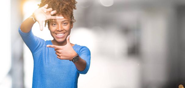 Hermosa mujer afroamericana joven sobre fondo aislado sonriendo haciendo marco con las manos y los dedos con la cara feliz. Concepto de creatividad y fotografía
. - Foto, imagen