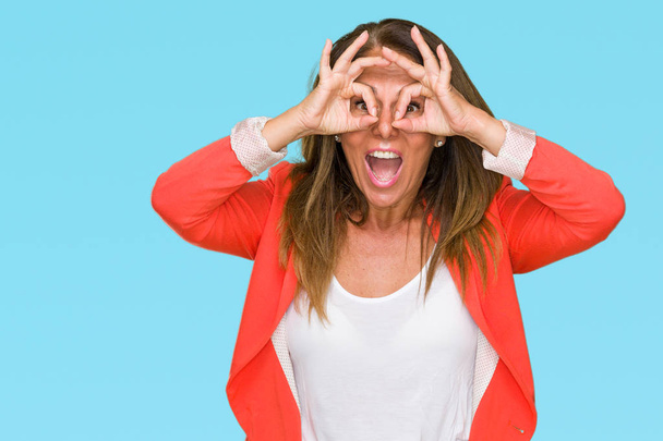 Beautiful middle age business adult woman over isolated background doing ok gesture like binoculars sticking tongue out, eyes looking through fingers. Crazy expression. - Photo, Image