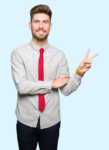Young handsome business man smiling with happy face winking at the camera doing victory sign. Number two. - Photo, Image