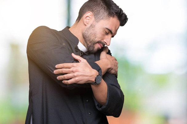 Jonge christelijke priester over geïsoleerde achtergrond knuffelen zichzelf gelukkig en positief, glimlachend zelfverzekerd. Zelfliefde en zelfverzorging - Foto, afbeelding