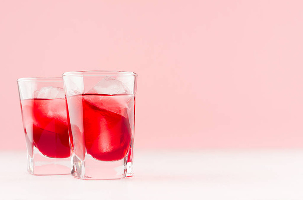 Red alcoholic liquor shots with ripe slice of strawberry with ice cubes on pastel soft light pink background, copy space. - Photo, image