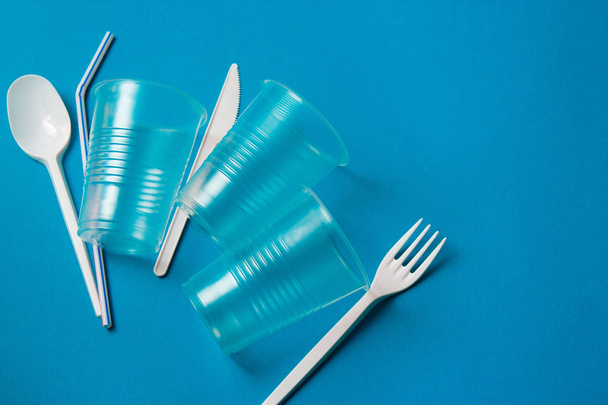 White single-use plastic knife, spoon, fork and plastic drink straws on a blue background. Say no to single use plastic. Environmental, pollution concept. - Foto, Bild