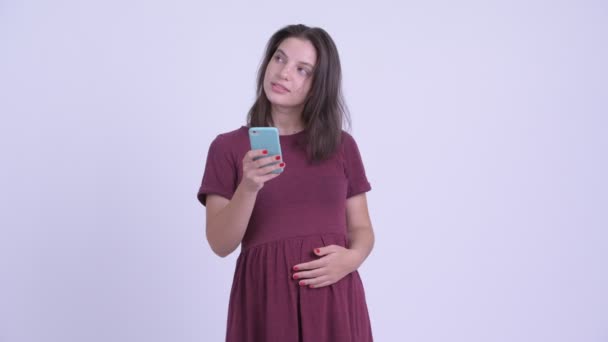 Happy young beautiful pregnant woman thinking while using phone - Footage, Video