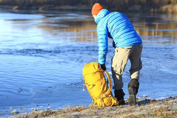 traveler with a backpack by the river / tourist guy on a northern hike, winter trip - Fotografie, Obrázek